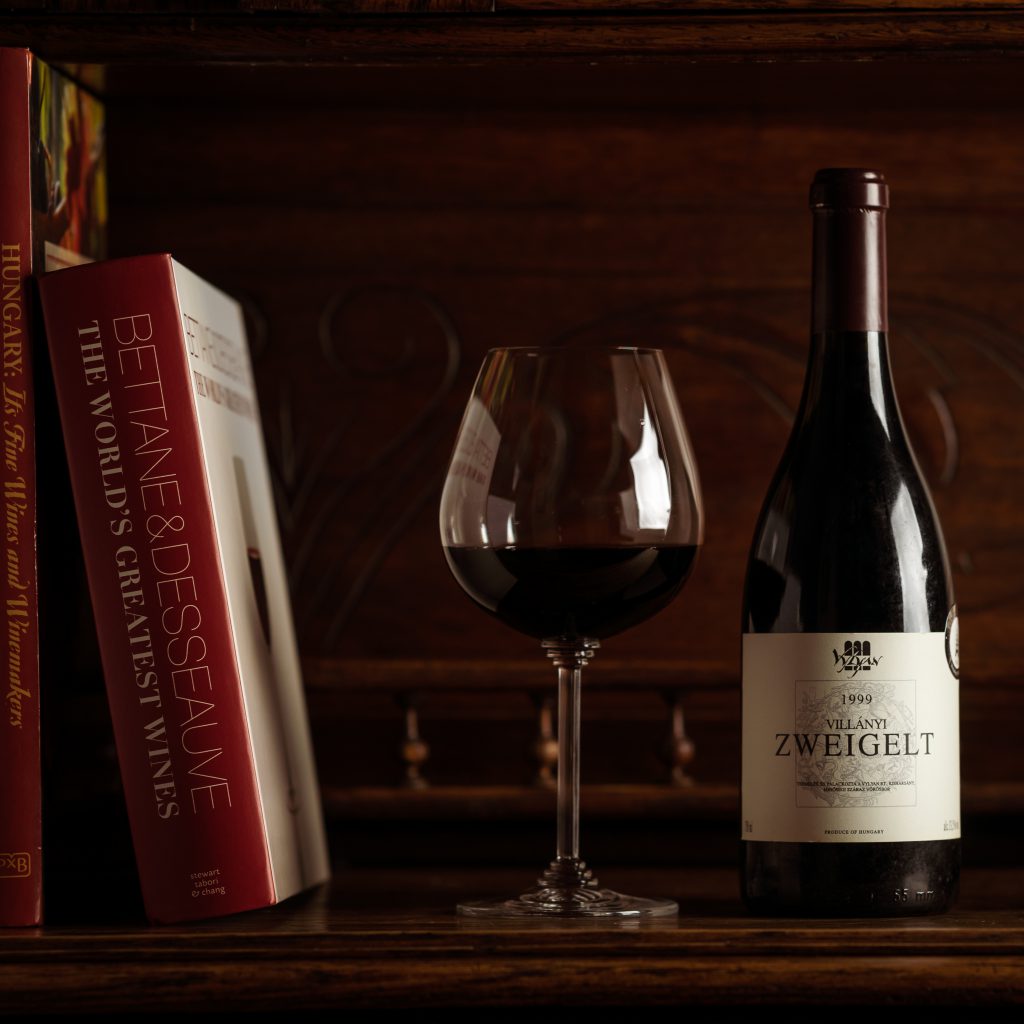 A Vylyan borászat jelenleg forgalomban lévő legidősebb bora, az 1999-es Zweigelt egy könyvespolcon üvegben és pohárban. 